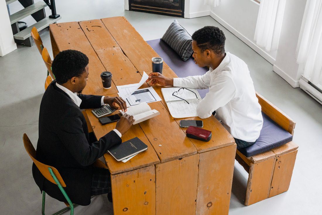 Two colleagues talk through documents and notes together at a wooden table before a meeting.