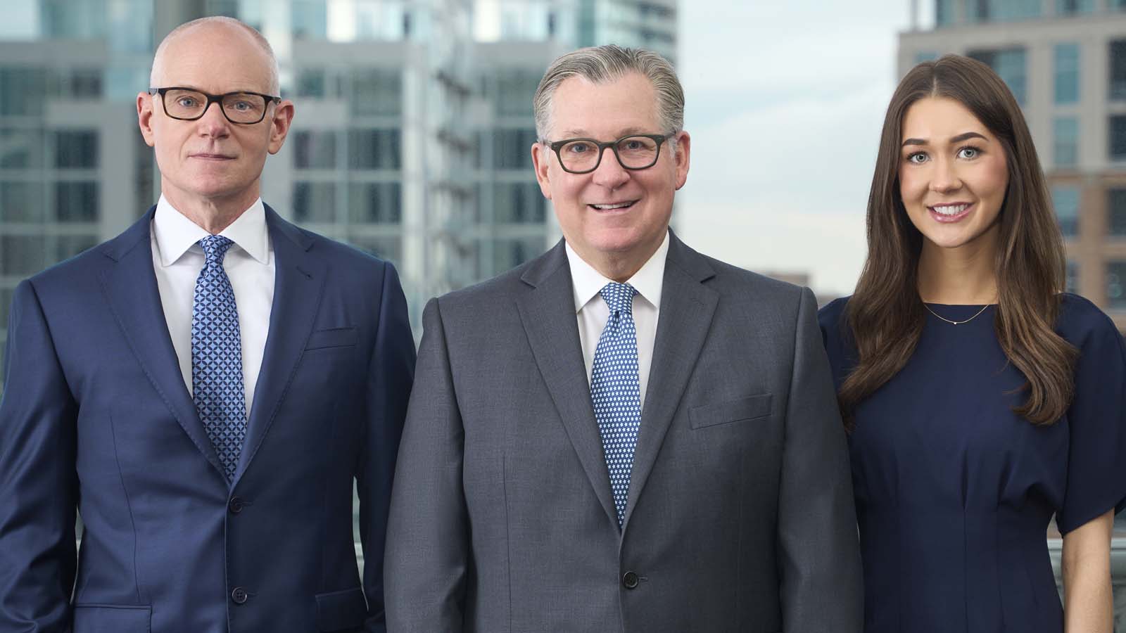 Three business professionals in suits standing together outdoors with New York City high-rises visible behind them.