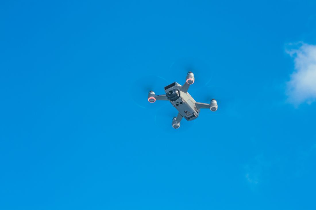 Small consumer drone hovering against a clear blue sky with light clouds