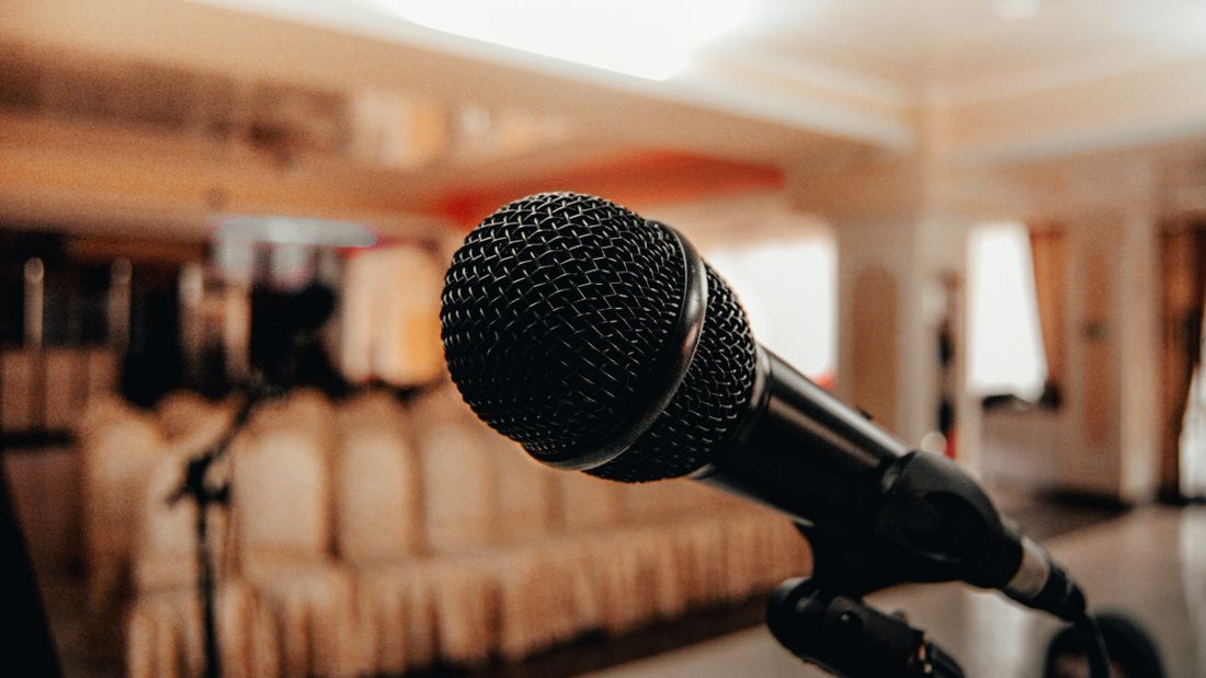 A black microphone on a stand positioned in a bright, spacious conference room with rows of empty chairs.