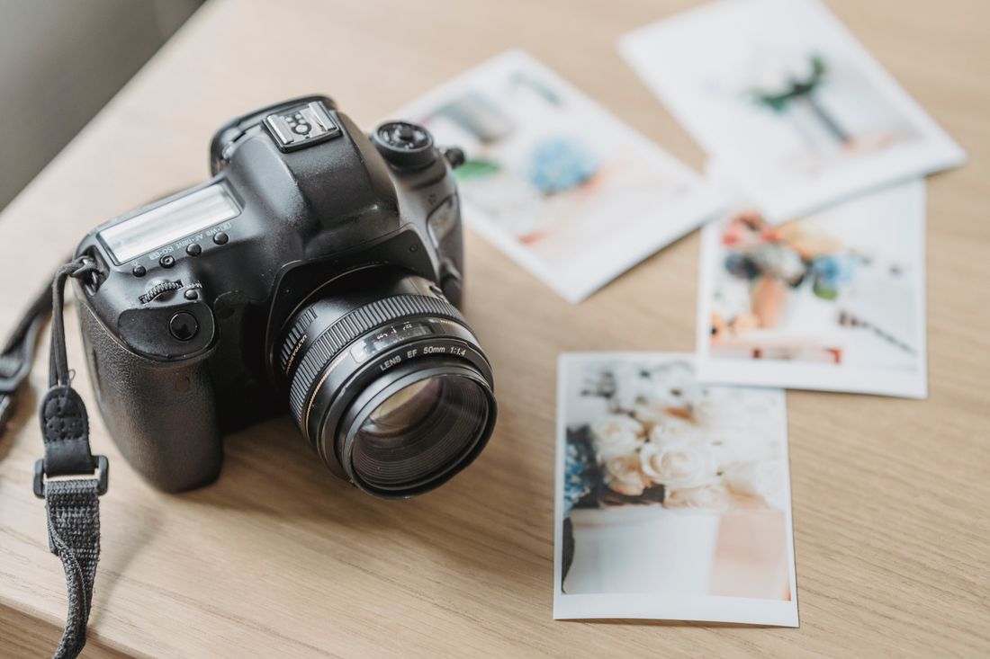 A professional camera resting on a desk beside a spread of printed photographs, representing an accumulating photo library