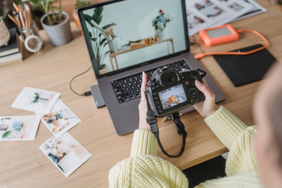 Overhead view of a photographer reviewing camera images at a desk next to a laptop and a stack of printed photos.