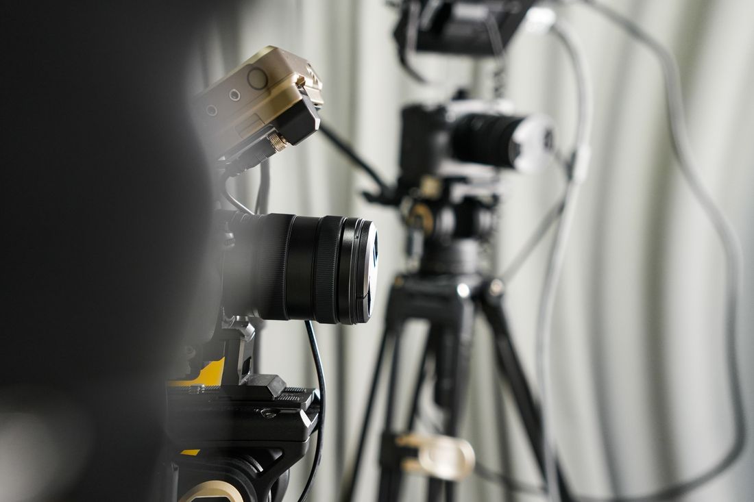 Close-up of professional video cameras mounted on tripods in a studio, cables and lighting visible in the background.