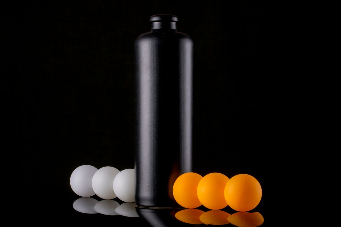 A matte black cylindrical product lit against a dark background with orange spheres beside it
