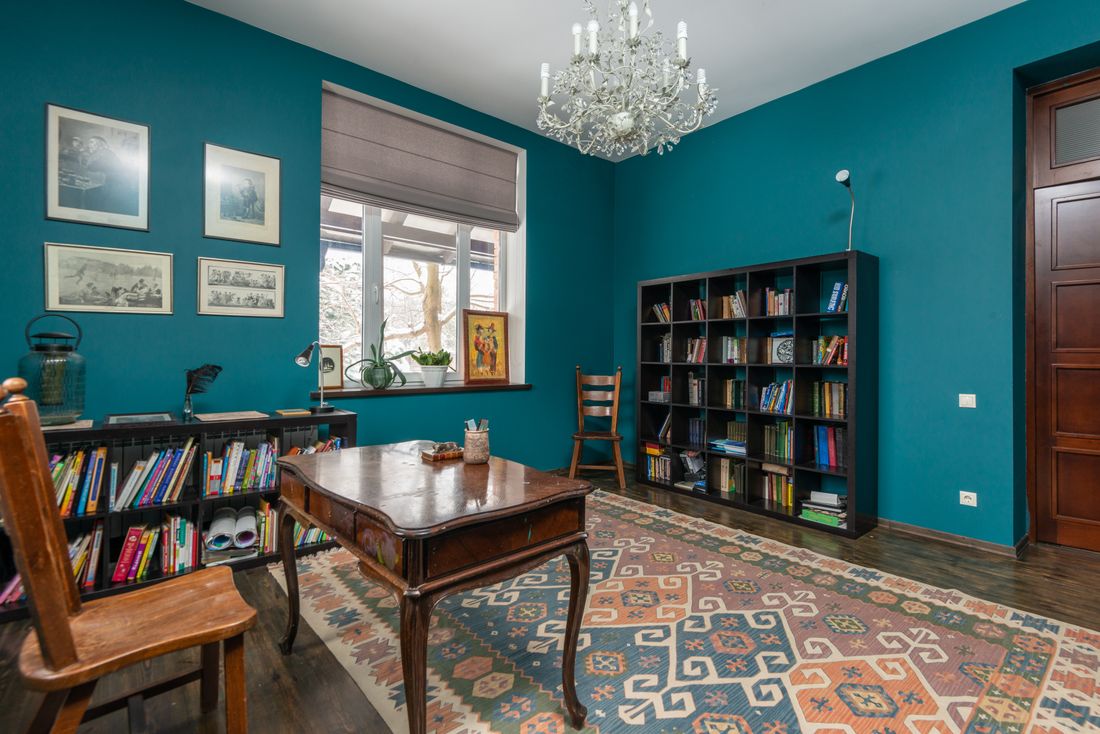 A blue-walled study with floor-to-ceiling bookshelves, a writing desk and a patterned rug