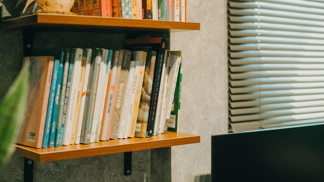 A close view of well-used books standing on a plain wooden wall shelf