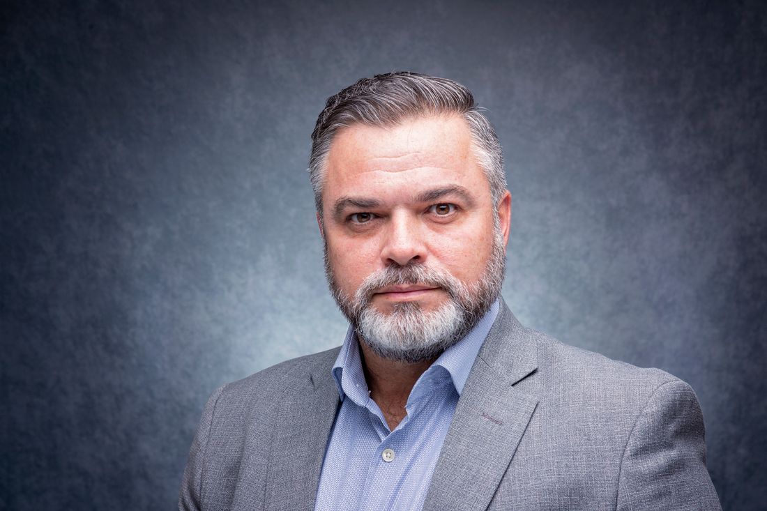 Formal studio portrait of a businessman in a gray suit against a neutral gray background, the kind of even, restrained lighting an annual-report portrait calls for.
