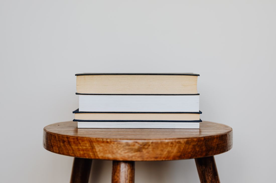 Small stack of three hardcover books on a wooden stool against a plain wall