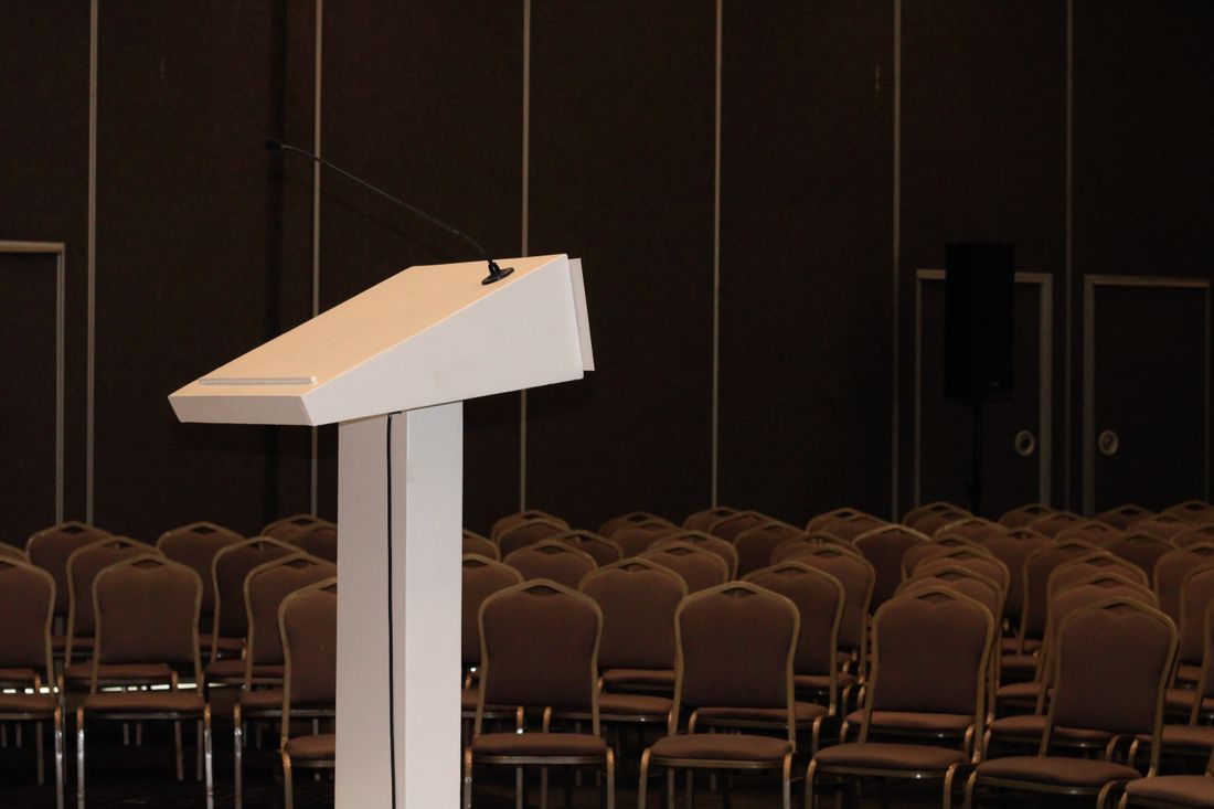 Empty conference room podium with a microphone facing rows of unoccupied chairs