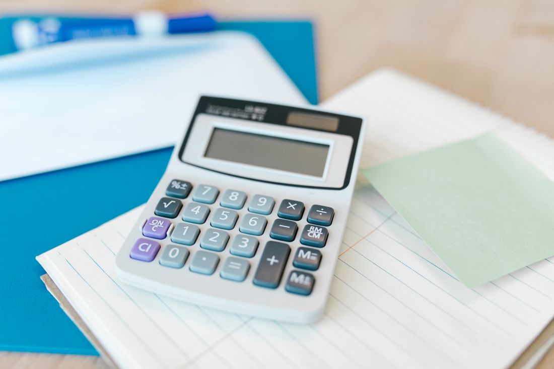 A calculator resting on a notepad beside a folder on a plain desk, set up for running cost comparisons.