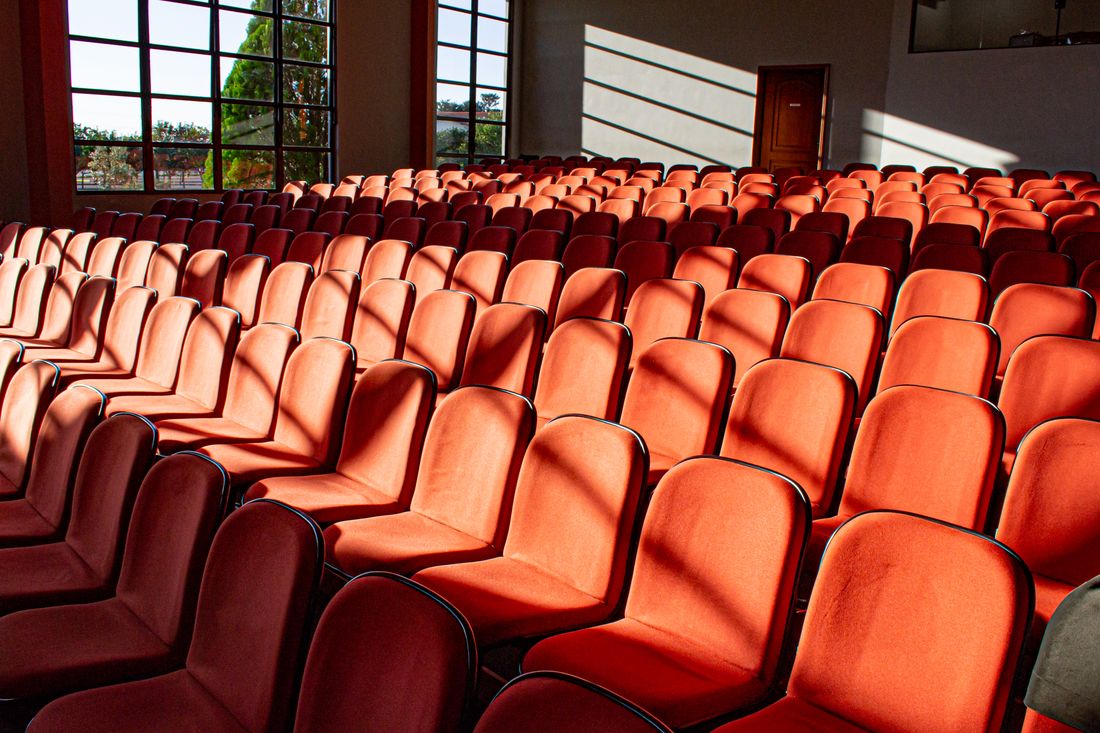 Rows of empty red auditorium chairs in sunlight.
