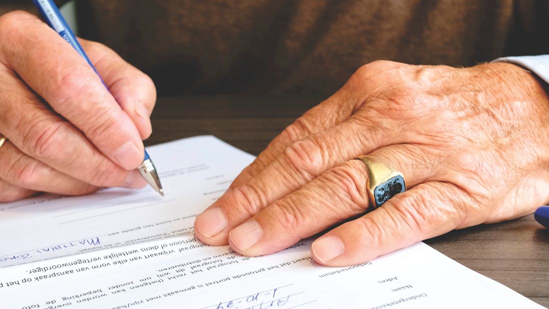 A close-up of a hand signing a printed document at a desk.