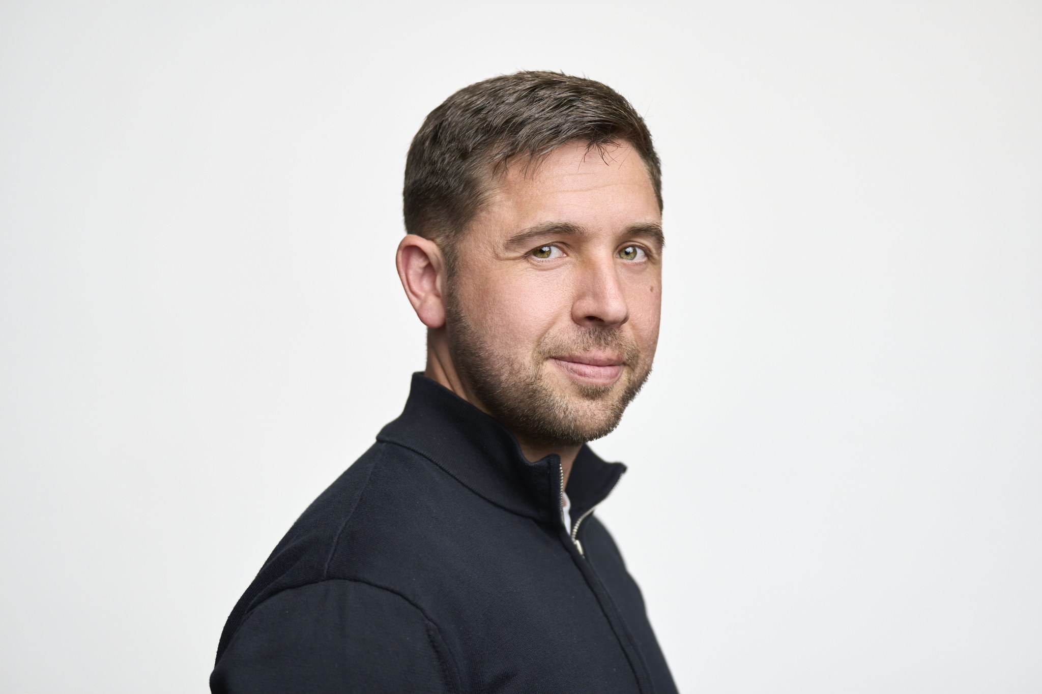 Man in dark zip sweater in three-quarter profile against white background.