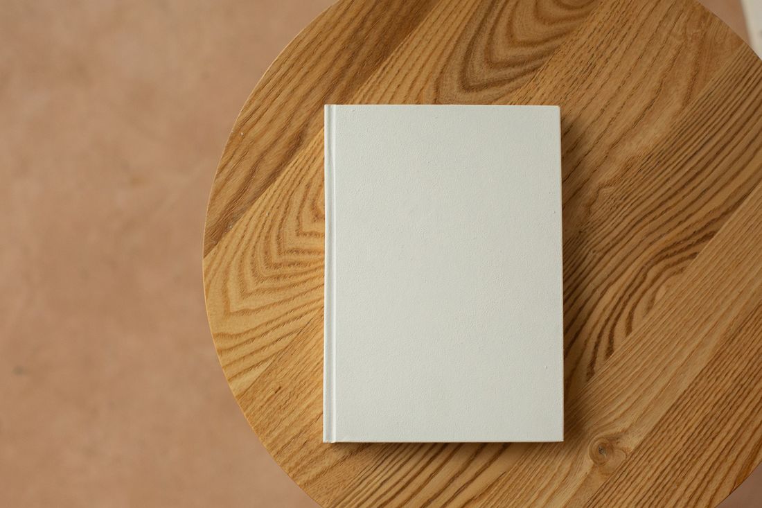 A blank white hardcover notebook lying closed on a round wooden table, seen from above.