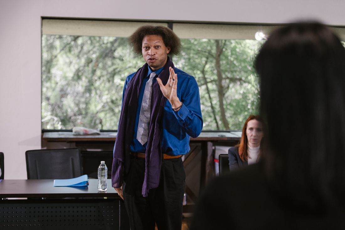 A professional in business-casual attire gesturing while speaking to a small group indoors.