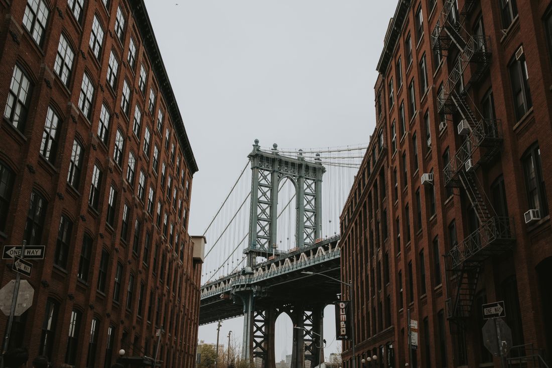 View of the Manhattan Bridge framed by red brick warehouse buildings on a Dumbo, Brooklyn street