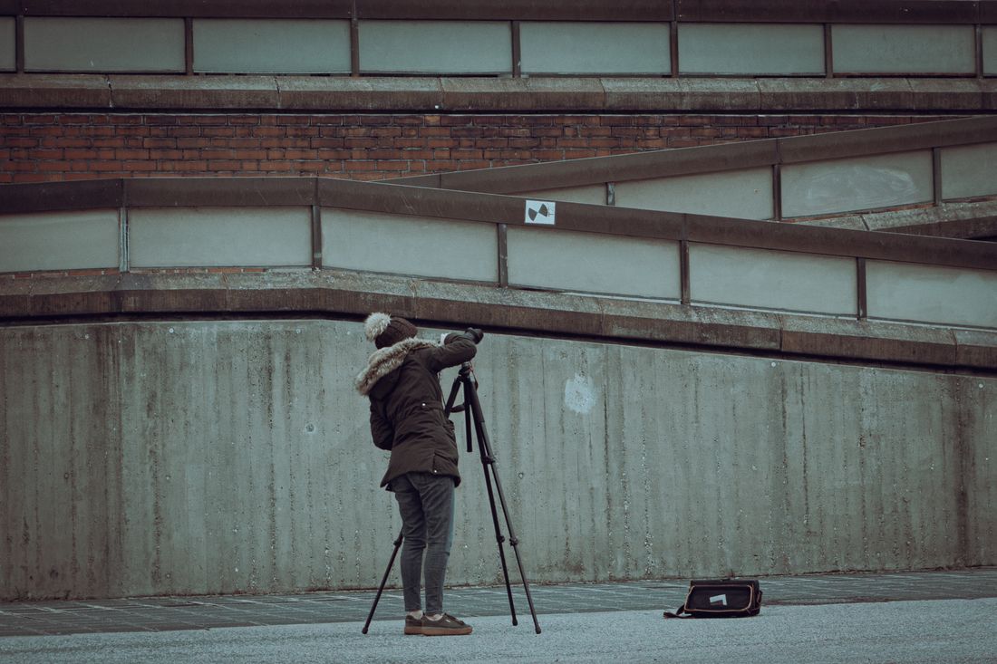 Photographer in winter clothing setting up a camera on a tripod on an urban street