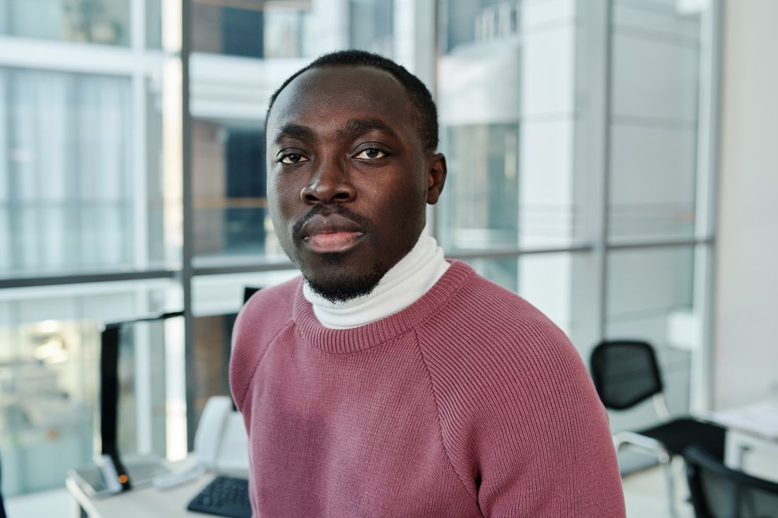 A close portrait of a man in a business-casual sweater in a bright office, looking directly at the camera with an approachable expression.