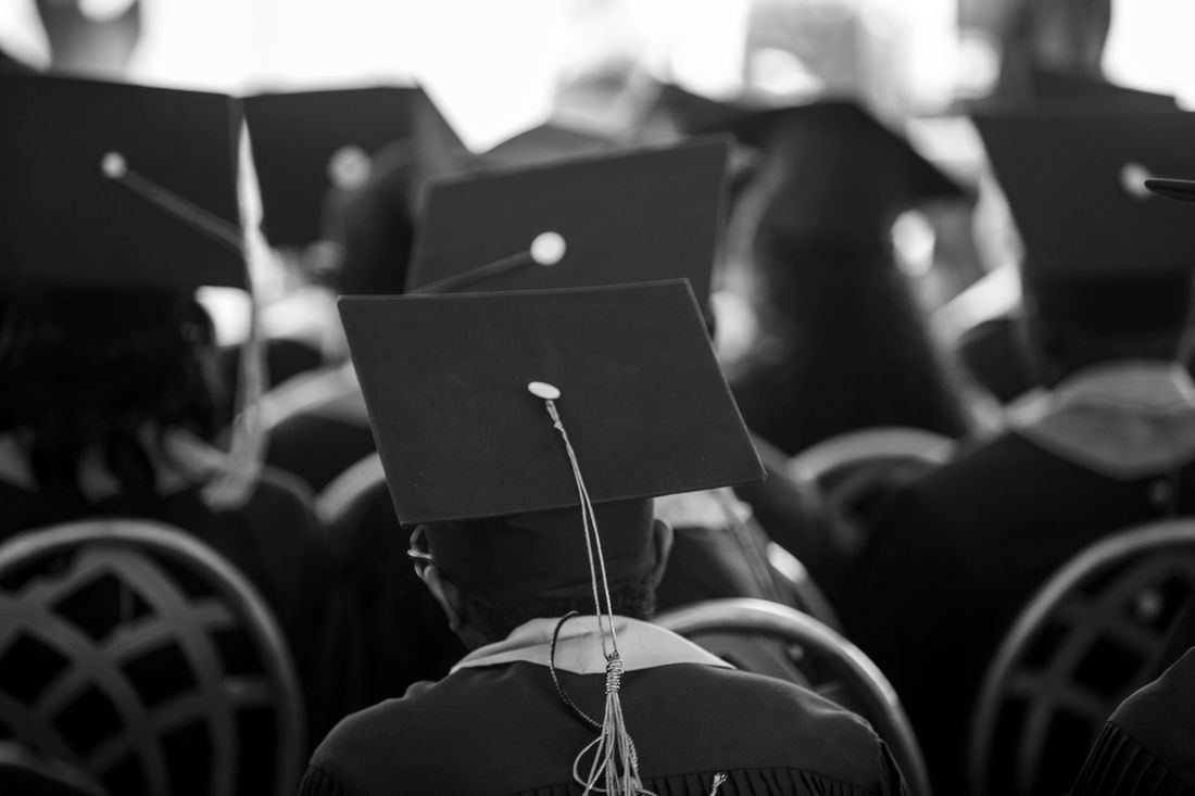 Rows of graduates in caps and gowns seen from behind, seated closely together, with mortarboards and tassels in soft focus fading into the background.