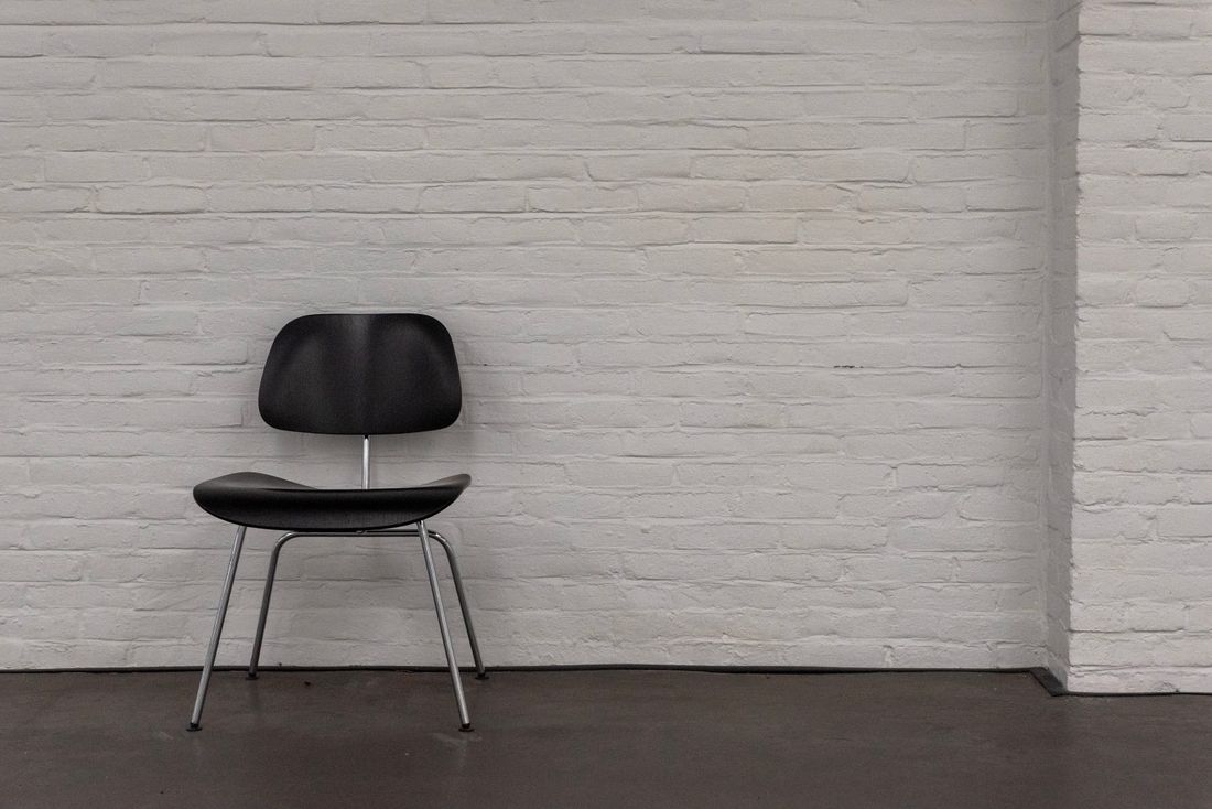 A single chair set against a plain white brick wall, an empty backdrop prepared for an on-camera segment.