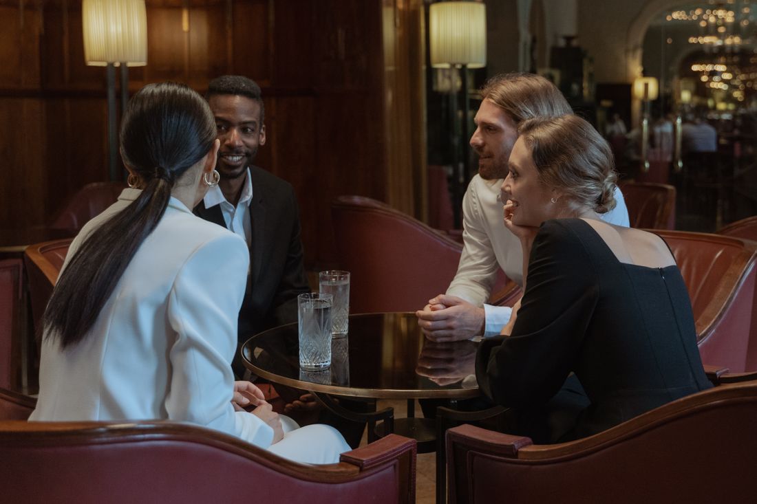 Four adults in business clothing having a natural conversation around a small table in a warmly lit lounge.