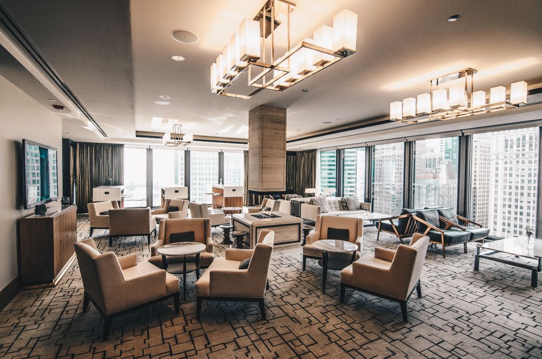 An empty upscale lounge with arranged chairs, small tables, large windows, and a city view beyond the glass.