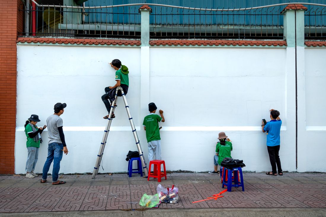 A group of volunteers on ladders painting a long exterior wall white