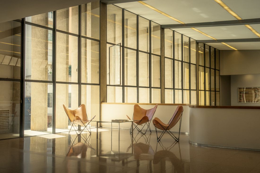 A sunlit lounge area with leather butterfly chairs and floor-to-ceiling windows in a shared workspace.