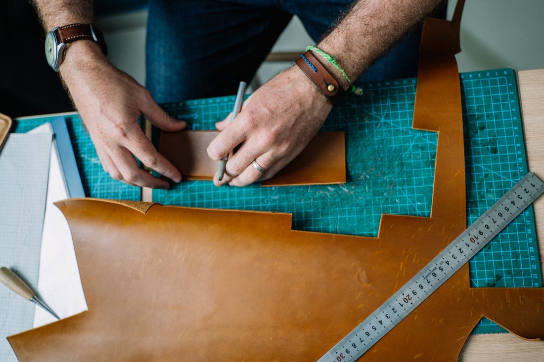 A close-up of hands cutting and shaping a piece of material on a work mat with a marking tool.