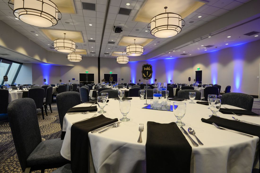An empty hotel ballroom set with round tables and place settings, prepared ahead of a formal evening event.