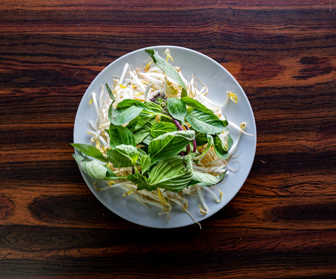 Overhead view of a single white plate holding a fresh herb and bean sprout salad, centered on a dark wooden restaurant table with nothing else in frame