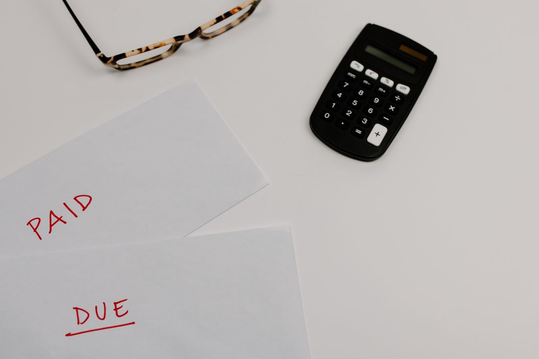 Financial paperwork marked “Paid” and “Due” next to a calculator on a desk, representing a production payment schedule.