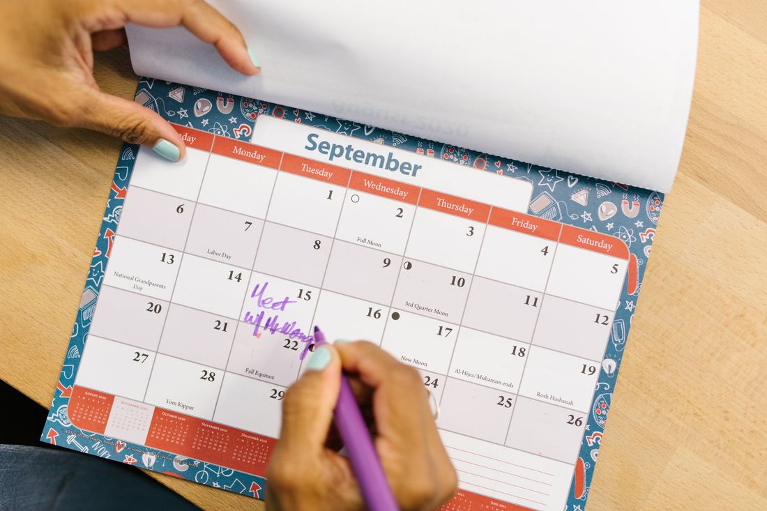 A hand marking a date on a wall calendar with a pen, representing a booking held on a studio's production schedule.