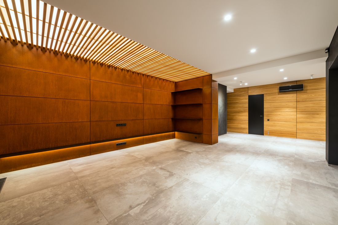 Empty modern hall with warm wood wall paneling, recessed ceiling lights, and polished concrete floor