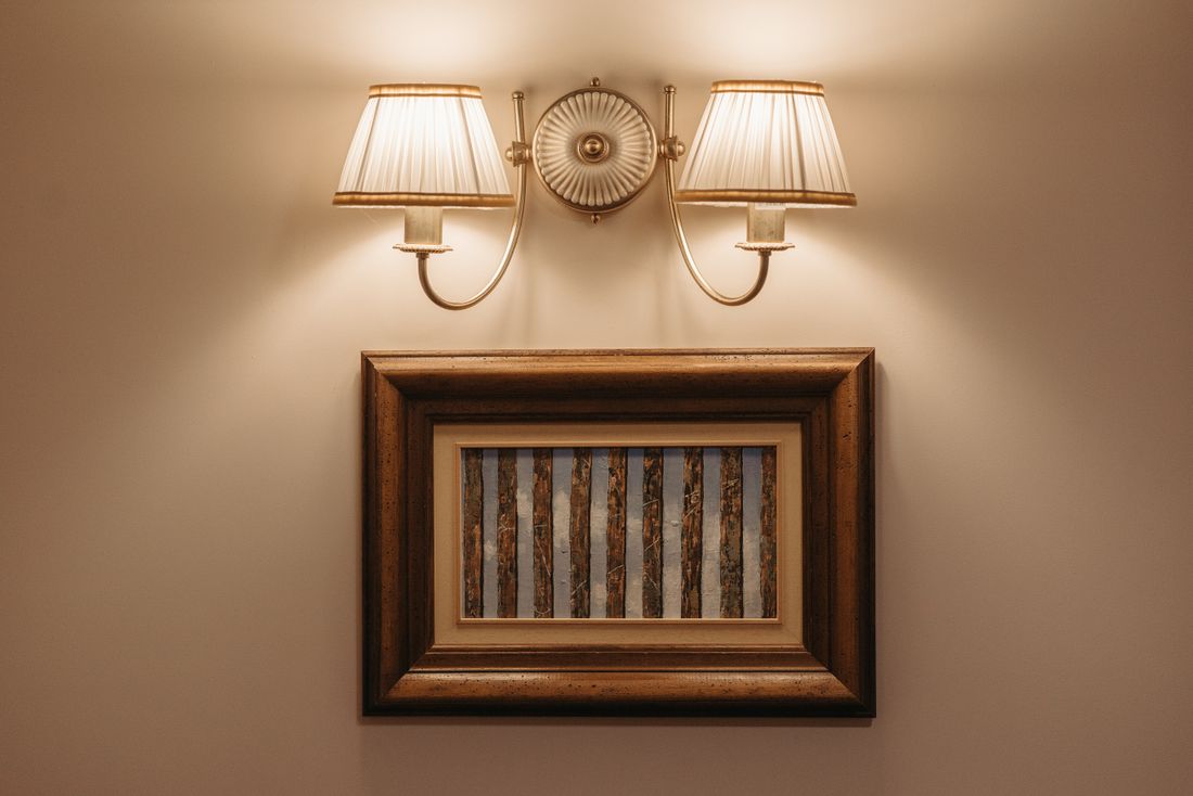A softly lit wall sconce illuminating a framed piece on a plain wall, evoking how a donor wall or plaque needs to be lit and photographed cleanly.