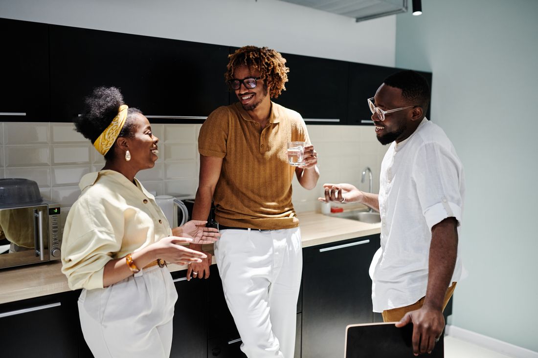 Three coworkers laughing together in a bright office kitchen during a break.