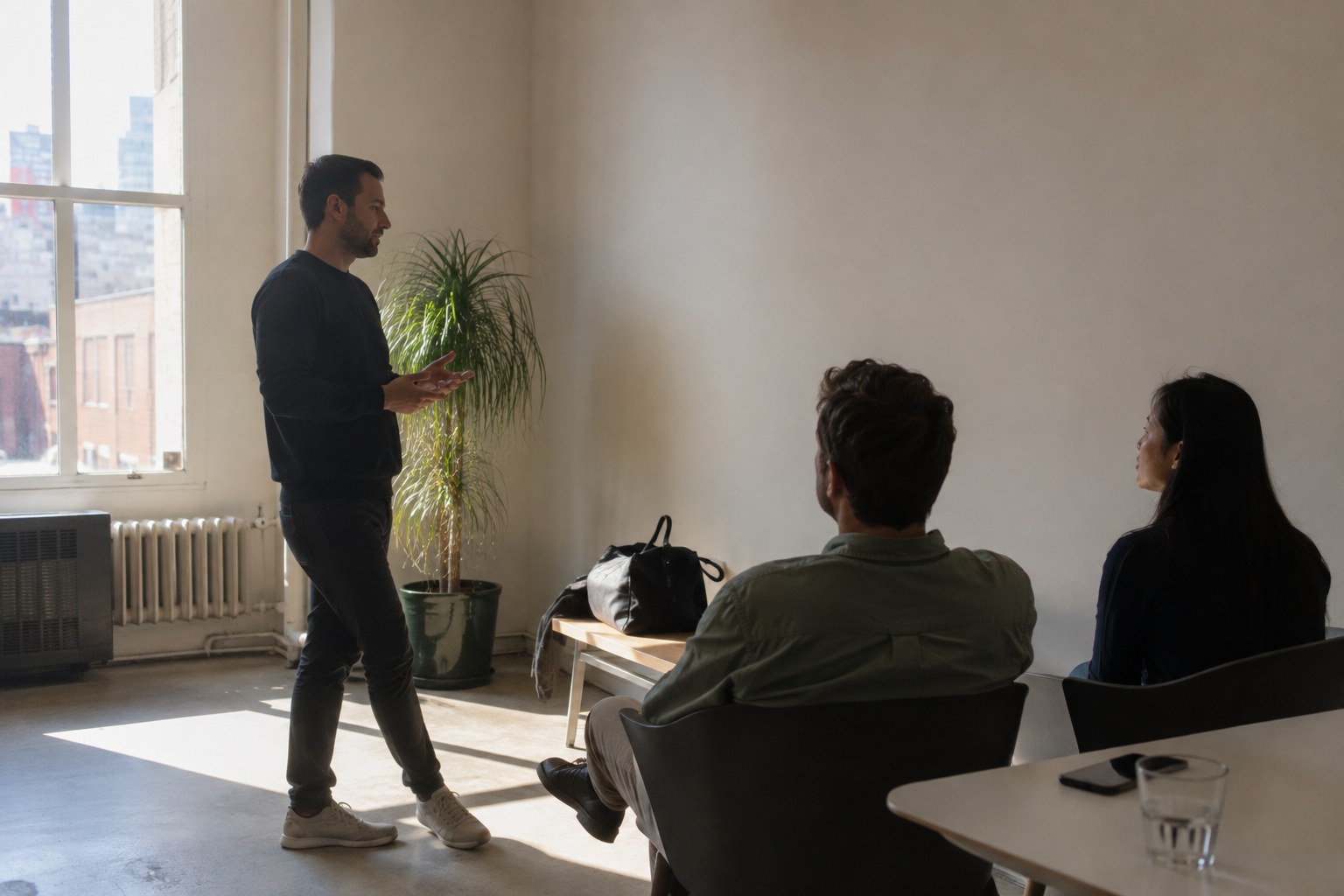 A speaker gestures while presenting to colleagues in a bright loft office setting.