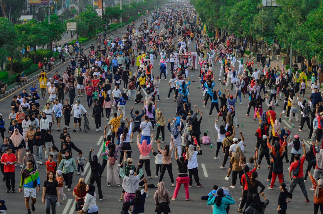 An elevated view of a large crowd of people walking, jogging, and stretching along a closed city street on a bright morning.