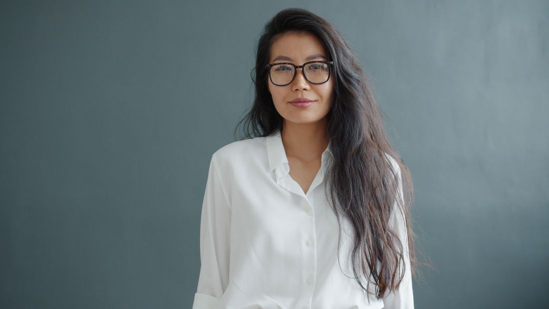 A woman in a white collared blouse and glasses photographed head-and-shoulders against a plain gray backdrop, calm direct expression, typical headshot framing.