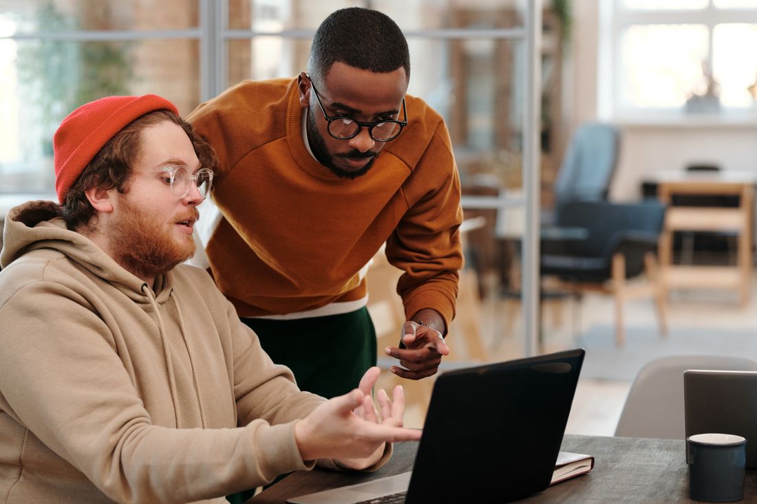 Two colleagues in casual clothing look together at a laptop screen during a focused discussion in a bright office.