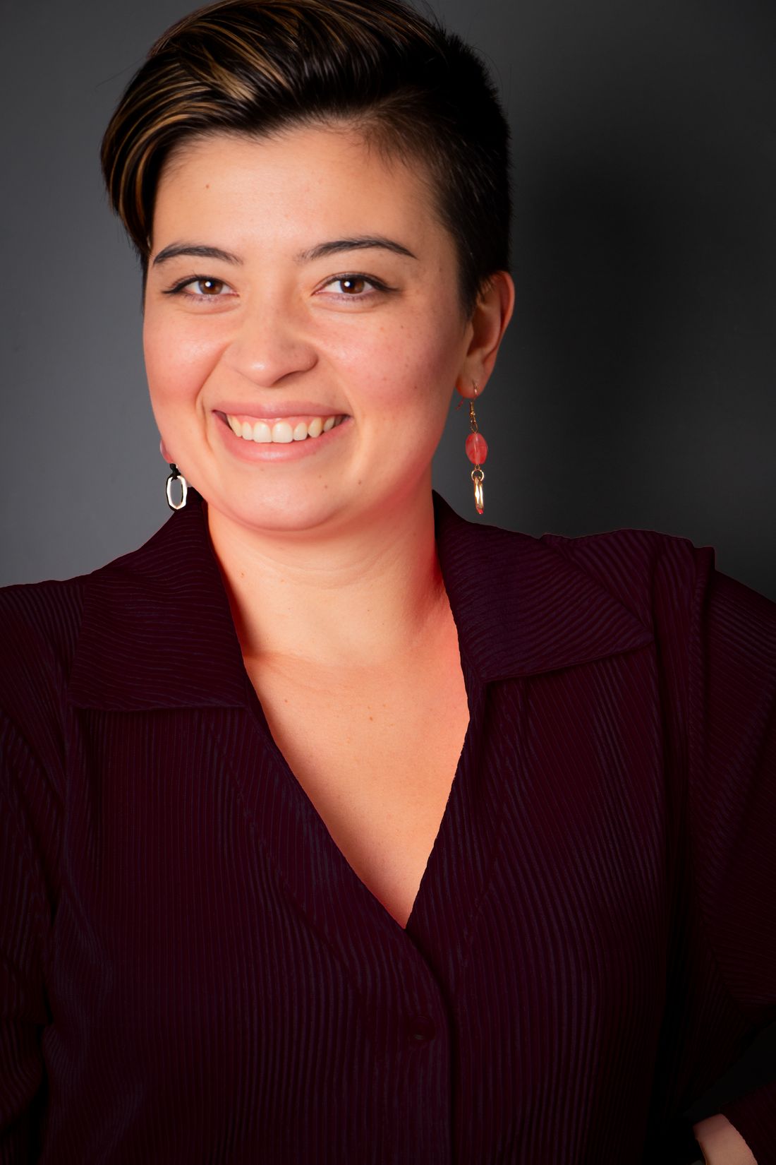 A close studio-style portrait of a smiling woman against a plain gray background, soft even light.
