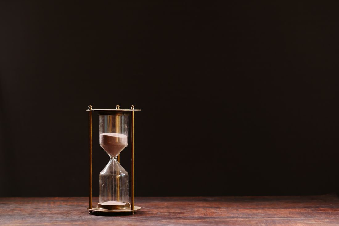 A brass hourglass with sand running low, set against a dark background on a wooden table.