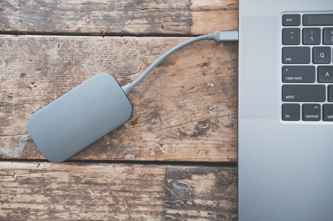 A portable external hard drive connected by cable to a laptop, resting on a weathered wooden desk.