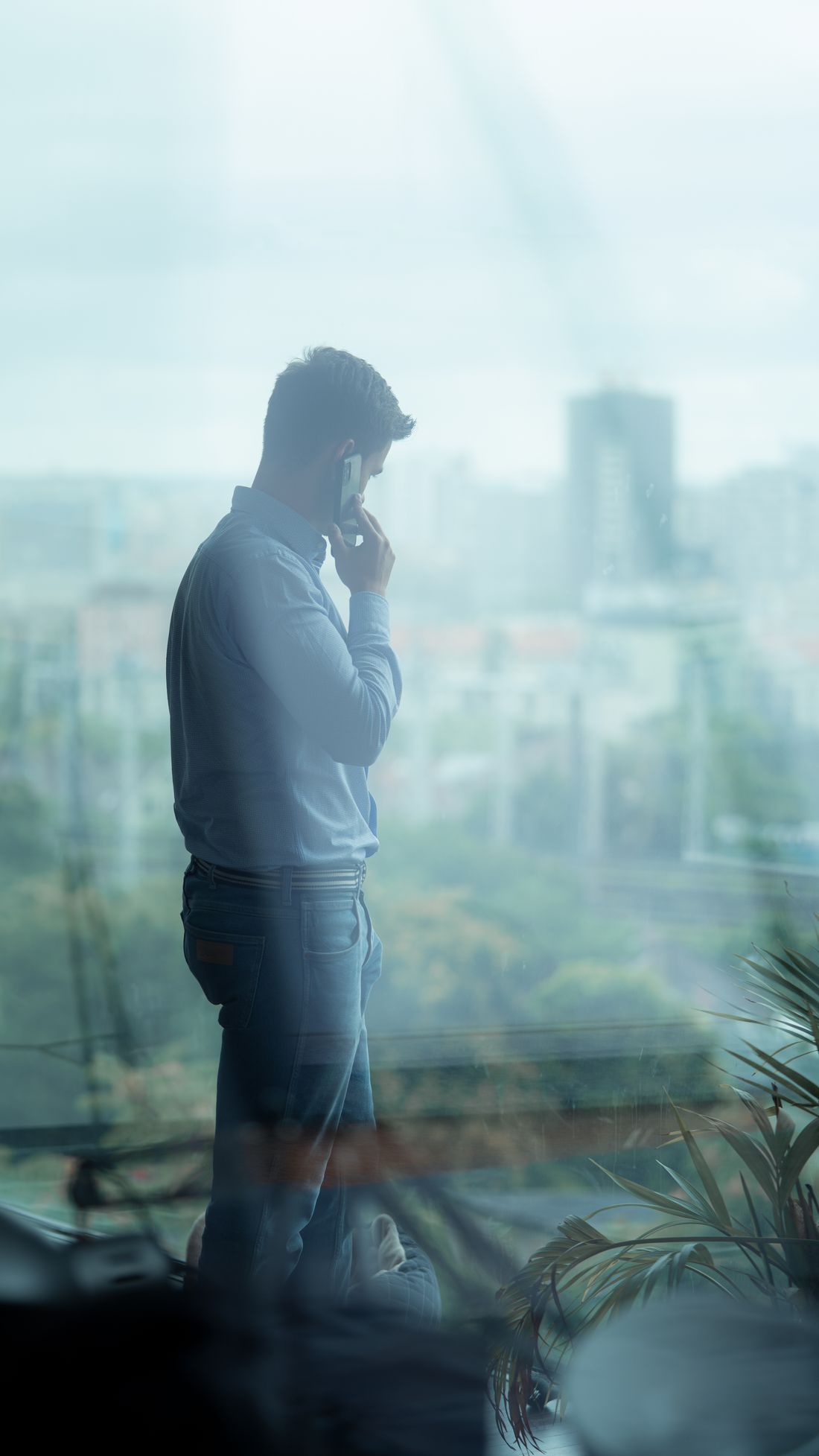 Side profile of a businessman on a phone call inside an office with a cityscape view.