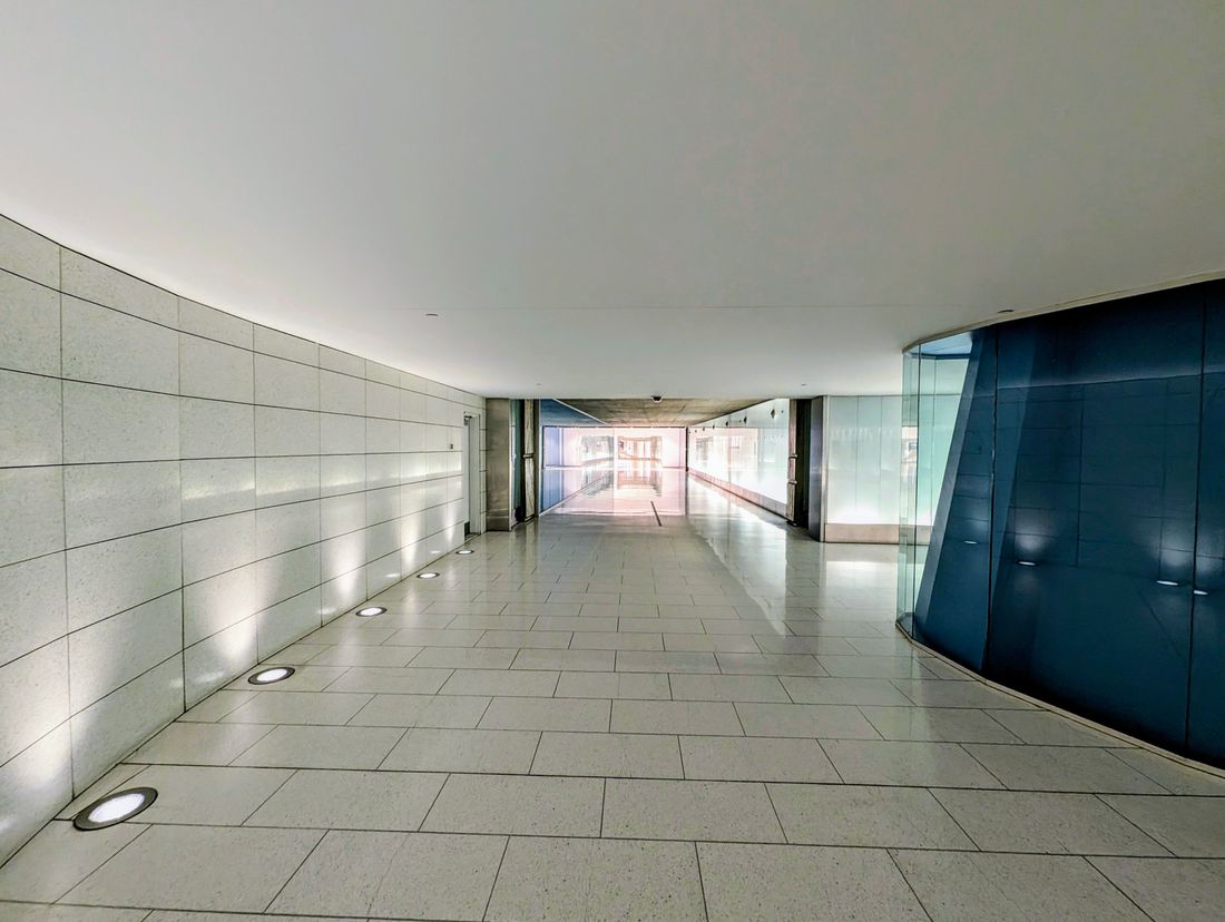 An empty, curved modern corridor with a polished tile floor and glass and glossy panel walls, nobody present.