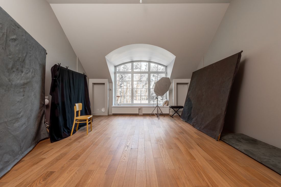 Empty photography studio with plain dark fabric backdrops, a single wooden chair, and a softbox light on a stand near a window, no people in frame.