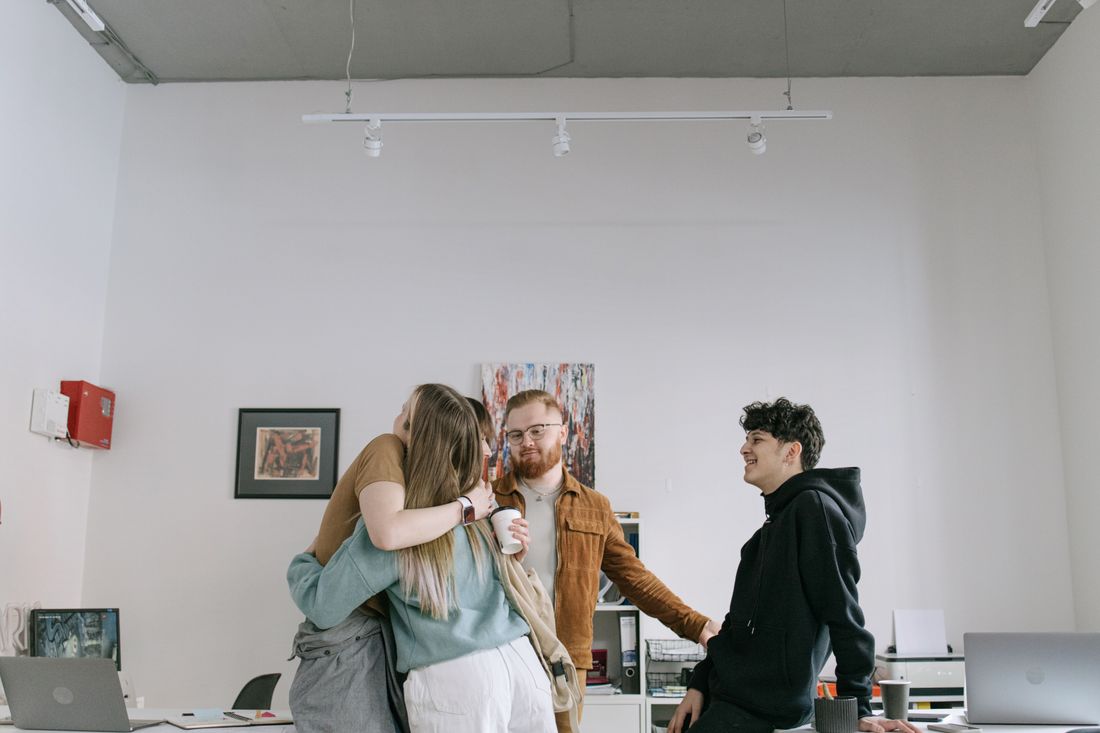 A small group of colleagues share a warm group hug and smile at each other in a bright, modern office.