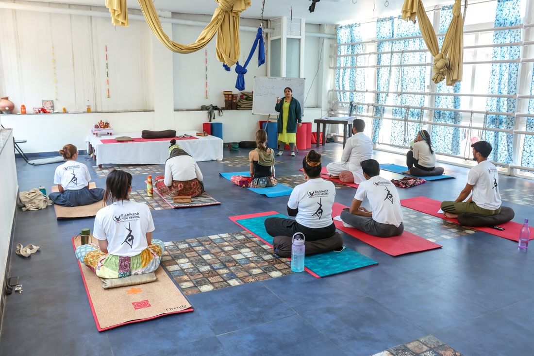 Instructor leading a small group yoga class in a bright studio, students seated on mats facing the front