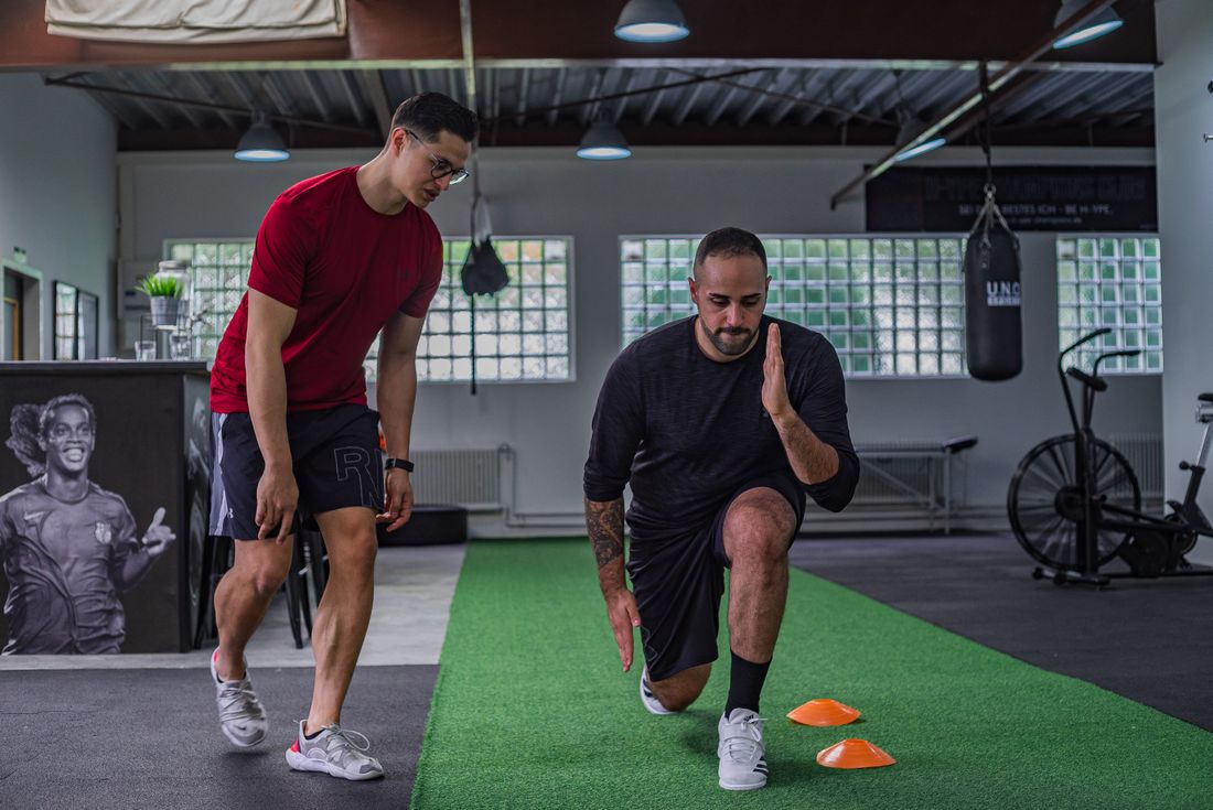 A coach guiding a client through a movement drill in a fitness studio, both focused on technique