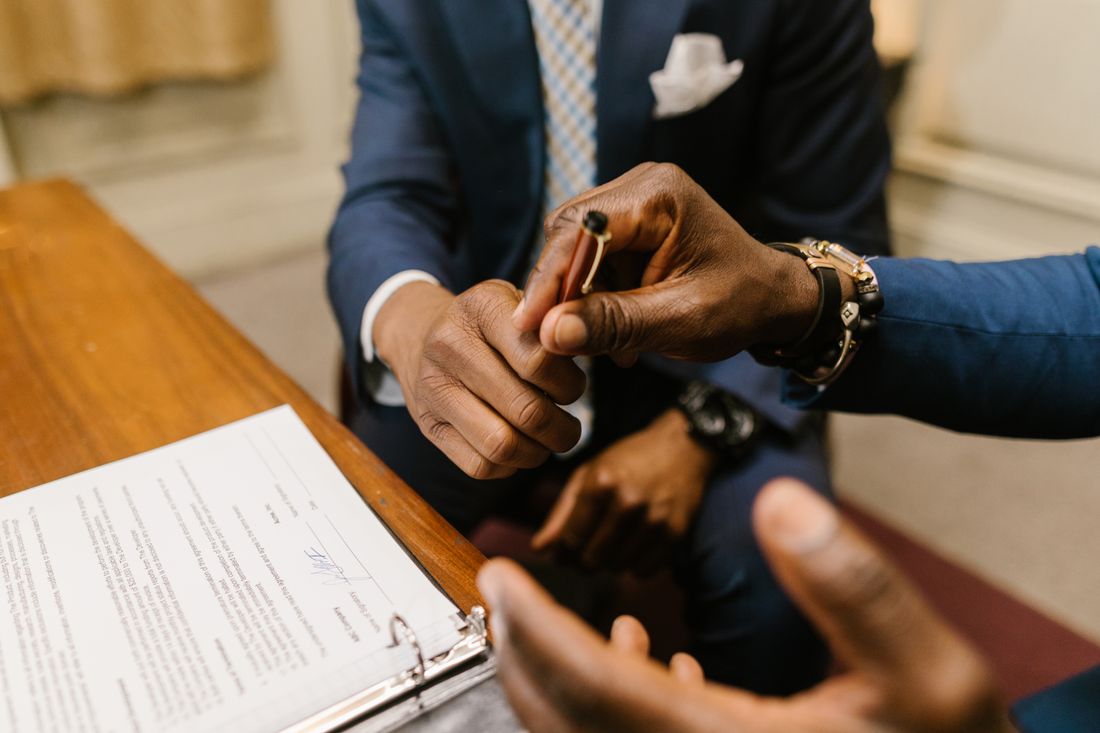 Close-up of one businessperson handing a pen to another to sign a document across a desk.